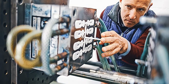 Engineer closely inspecting an open injection mould in a factory setting, adjusting mould cavities to ensure precision and process control.