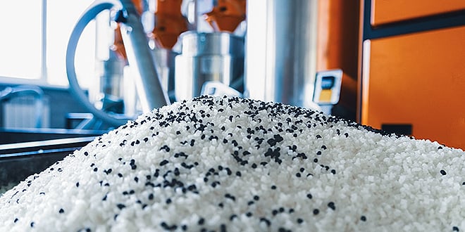 A pile of white plastic granules mixed with black particles in a modern production facility, symbolising durable and tough material compounds used in advanced manufacturing.