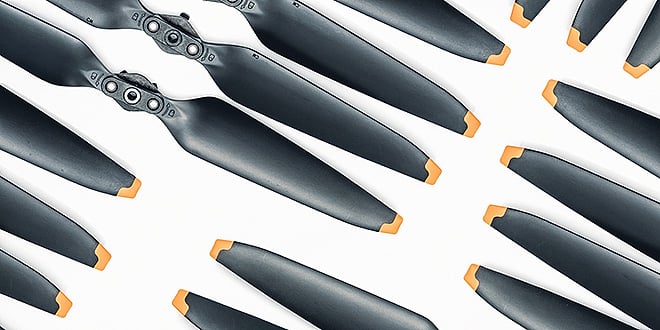 Multiple black aircraft propeller blades with orange tips arranged in rows, symbolising precision manufacturing and lightweight aerospace components.