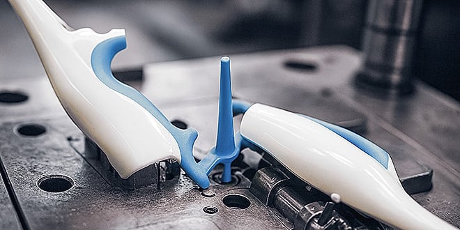Close-up of a plastic injection mould showing two moulded white and blue parts with a sprue, demonstrating reliable bonding in consumer goods production.