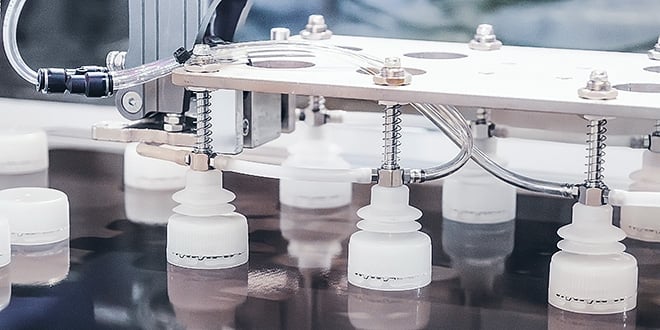 An automated robotic gripper with suction cups precisely handling white plastic caps on a production line, illustrating scalable packaging manufacturing.