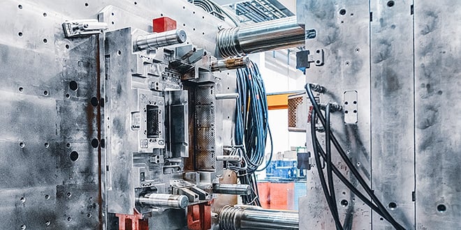 Close-up of an open metal injection mould inside a manufacturing machine, showing detailed cavity structures, cooling channels, and connected cables used for precise thermal control in plastic part production.