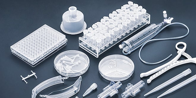 Assortment of transparent plastic medical components including syringes, pipettes, tubes, and lab trays, representing precision-moulded parts for healthcare applications.