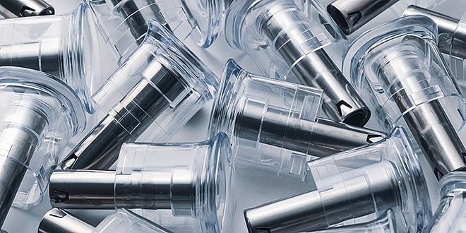 Pile of transparent plastic components with integrated metal nozzles, demonstrating high-precision multi-material injection moulding used in medical technology.
