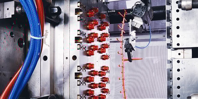 Close-up of an injection mould with multiple red plastic parts being produced, showing precision mould design and automated handling in an industrial manufacturing setup.