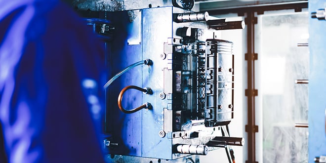 Injection mould with open halves revealing complex tool design, pipes, and connections for producing multi-component plastic parts in an industrial environment.