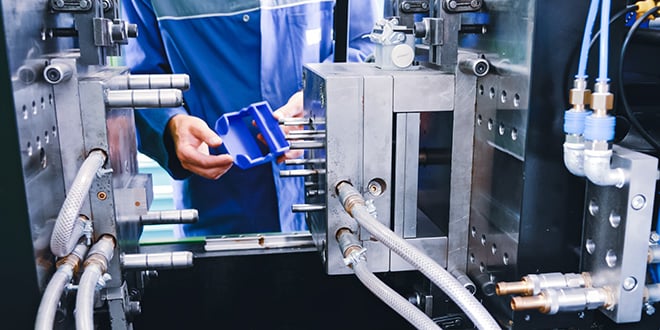 Technician inspecting a blue plastic part freshly moulded in an injection machine, demonstrating early validation and quality assurance in industrial production.