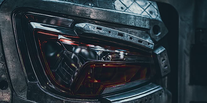 Detailed view of a metallic injection mold forming a red automotive taillight.