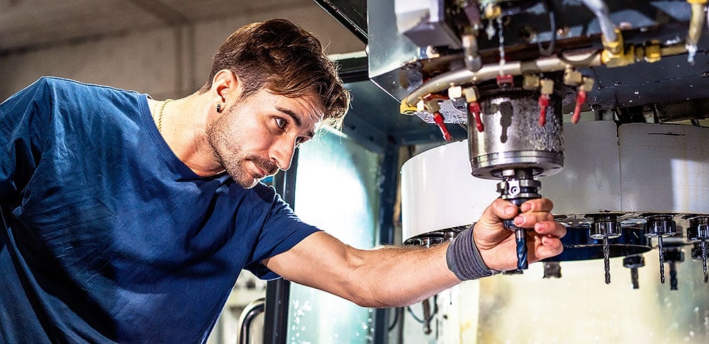 A focused technician in a blue shirt adjusts a tool on a CNC milling machine in a workshop.