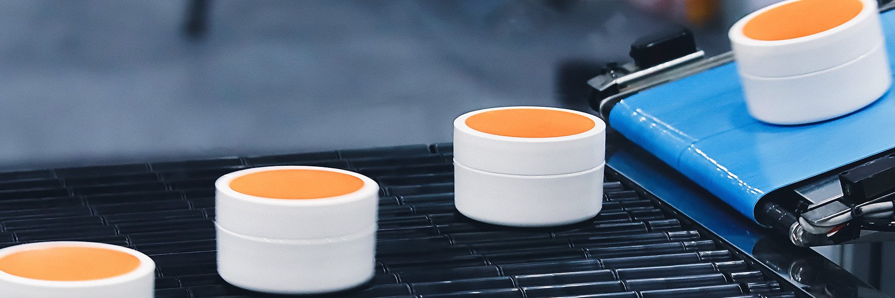 In the factory, cosmetic cream jars travel along a conveyor belt.