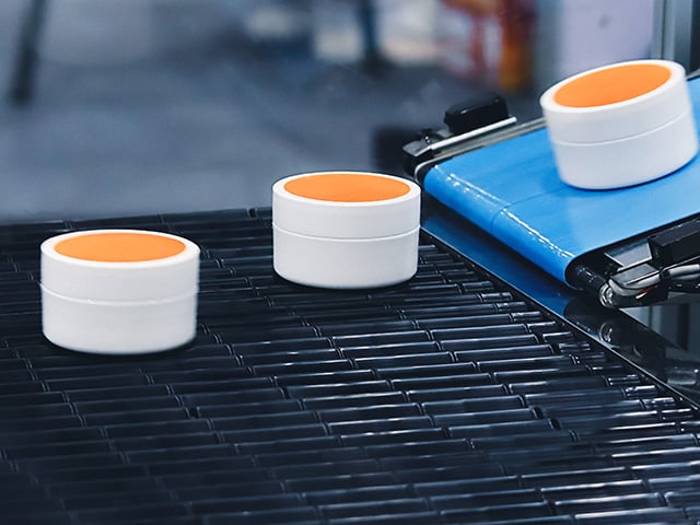 In the factory, cosmetic cream jars travel along a conveyor belt.
